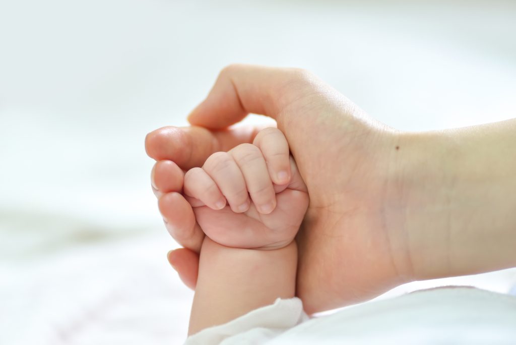 Mano de bebé agarrada por la mano de su madre.