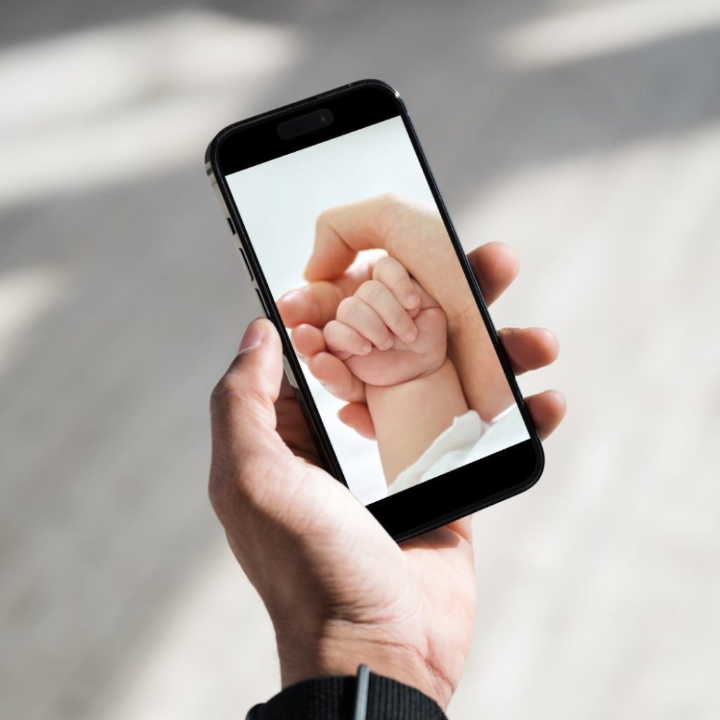 Imagen de una mano sosteniendo un móvil con una foto de una mano de bebé.